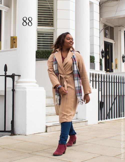 :hoto of me in a long, beige trench coat, jeans, and a scarf, walking down the road. The coat is from the Frankie x Oasis collaboration.