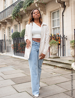 Photo of author in white jacket, white top and jeans, the perfect transitional clothing for autumn. She is smiling at the camera