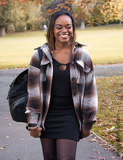 Photo of author in black T-shirt, black skirt, brown plaid shacket and a black backpack