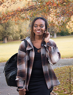 Photo of author in black T-shirt, black skirt, brown plaid shacket and a black backpack
