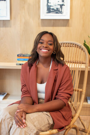 Author Jasmine Burke laughing in a rust blazer, sitting in a rattan chair