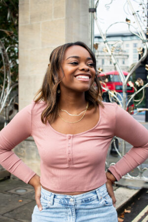 Author Jasmine Burke smiling in a pink top with her hands on her hips on a London street
